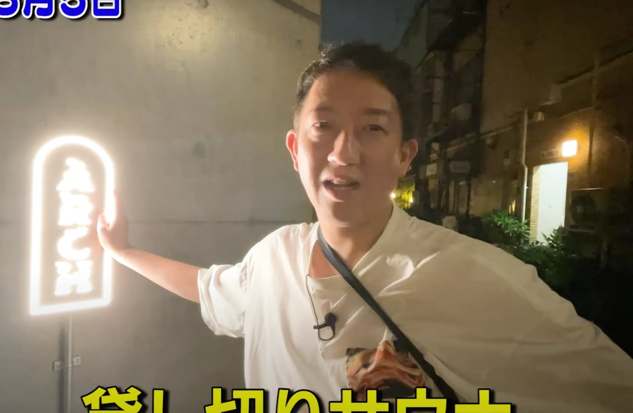 ARCH入口のネオンサイン脇に立つサバンナ高橋さん